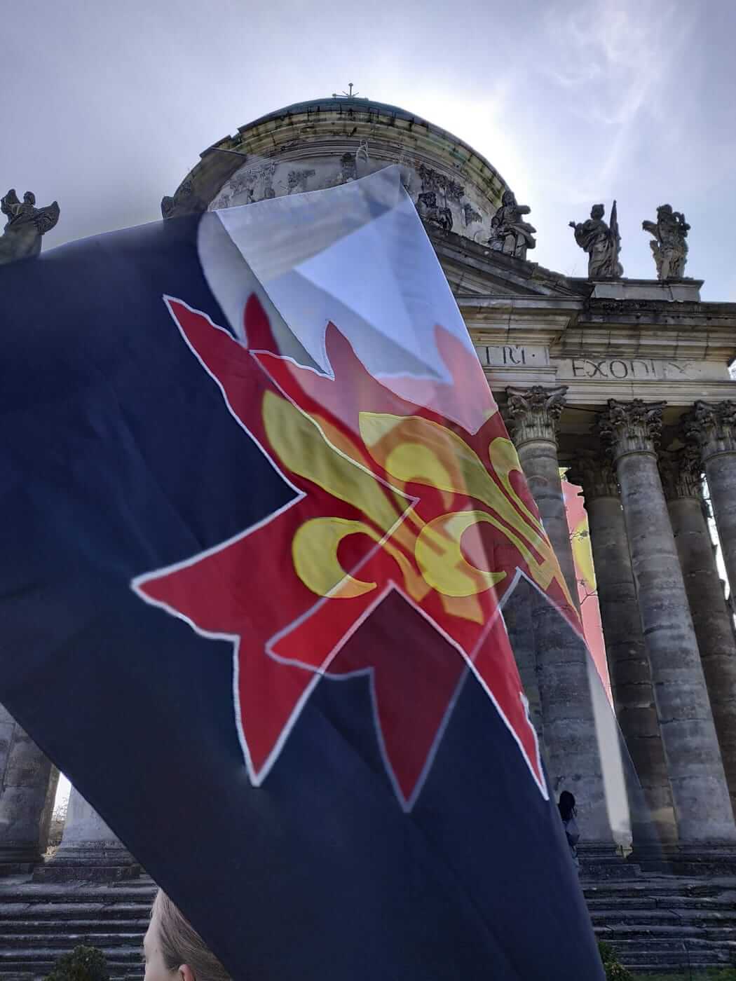 Прапор Буасан із червоним хрестом і золотою лілією перед храмом